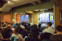 Image of someone giving a presentation to a large group of onlookers. 